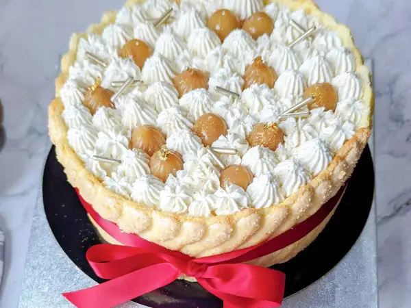 Magnifique recette charlotte : une mousse aérienne, des marrons glacés et une touche d'or comestible, le tout entouré d'une belle robe de biscuits cuillère et d'un ruban rouge.