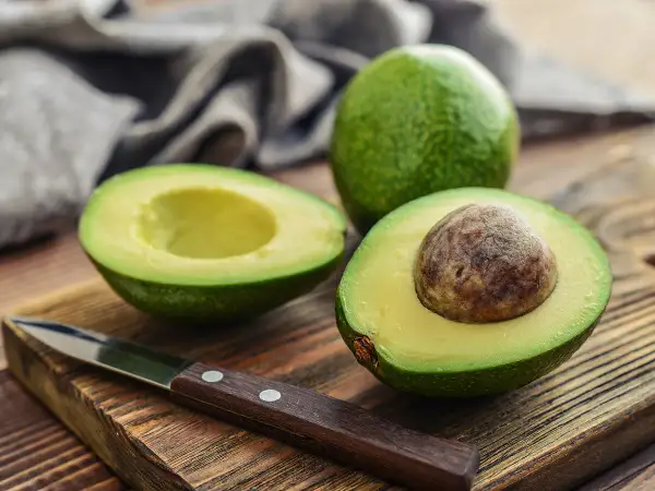 Un avocat coupé en deux sur une planche en bois, prêt à être préparé. Astuce pour empêcher un avocat de noircir sans citron.