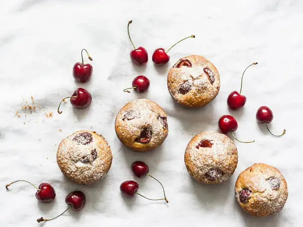 Financiers aux cerises saupoudrés de sucre glace, disposés avec des cerises fraîches sur un tissu blanc.