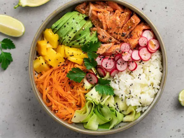 Un bol coloré avec saumon, avocat, mangue, carottes râpées, radis, courgette et riz blanc. Parfait pour des menus semaine famille équilibrés et savoureux.