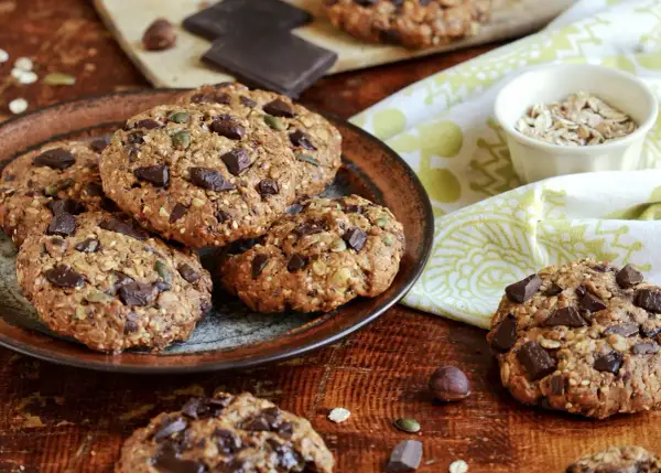 Gourmands cookies flocons d'avoine, parsemés de pépites de chocolat noir et de graines, sur une assiette rustique.