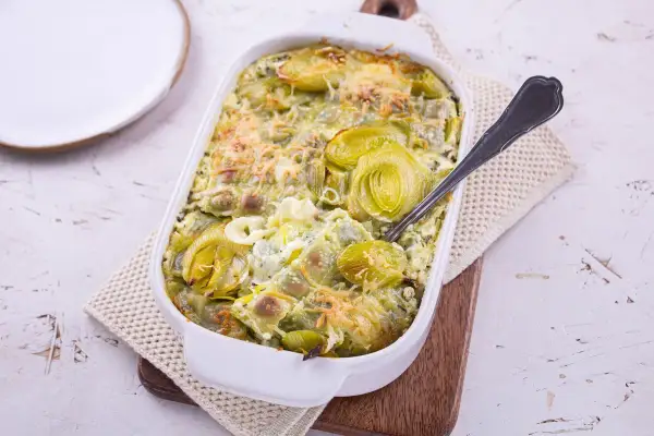 Plat gratiné de ravioles aux poireaux, une recette de Laurent Mariotte, servi dans un plat blanc avec une cuillère.