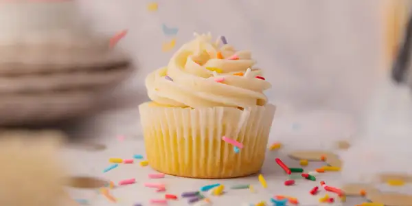 Un cupcake vanille avec glaçage crémeux et vermicelles colorés tombant. Une recette facile pour un goûter gourmand.