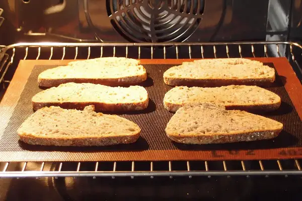 Six tranches de pain de campagne, prêtes pour la décongélation pain four, sur une plaque en silicone dans un four chaud.