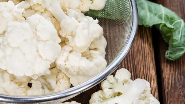Chou-fleur frais coupé en bouquets dans une passoire, prêt pour la cuisson. Eau froide ou chaude, le choix dépend de la recette.
