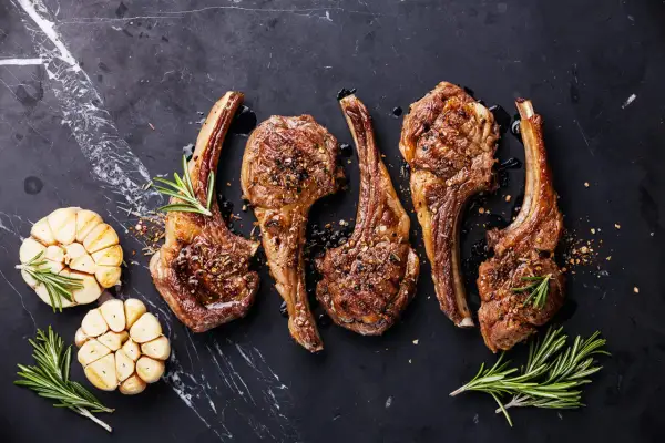 Quatre côtelettes d'agneau grillées, assaisonnées et garnies de romarin, avec des têtes d'ail rôties. La cuisson côtelette agneau parfaite.