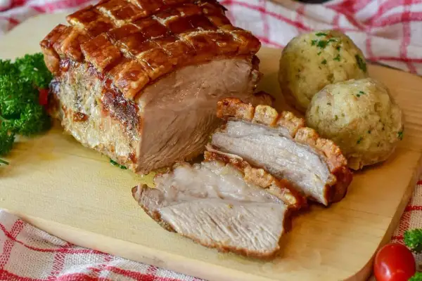 Rôti de porc croustillant, coupé en tranches, servi avec des boules de pain et du persil. Le temps de cuisson du rôti de porc est parfait.