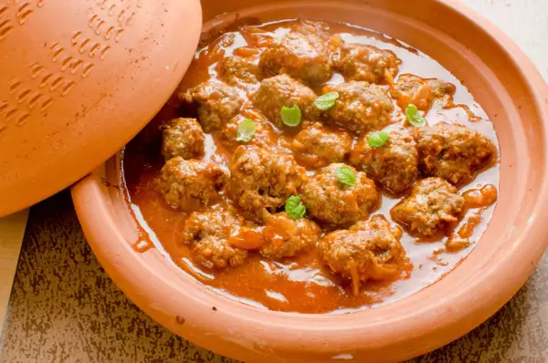 Un plat de tajine kefta, des boulettes de viande mijotées dans une sauce tomate épicée, garni de feuilles de menthe fraîche.
