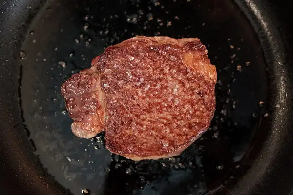 Un beau morceau de Black Angus en cuisson dans une poêle, avec des cristaux de sel qui fondent.