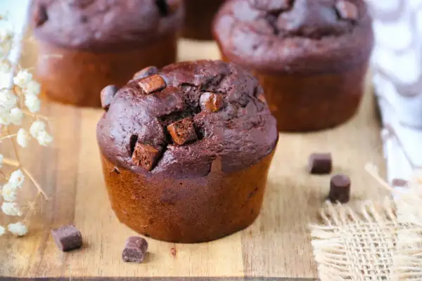 Gros plan sur un muffin banane chocolat moelleux, parsemé de pépites de chocolat, sur une planche en bois.