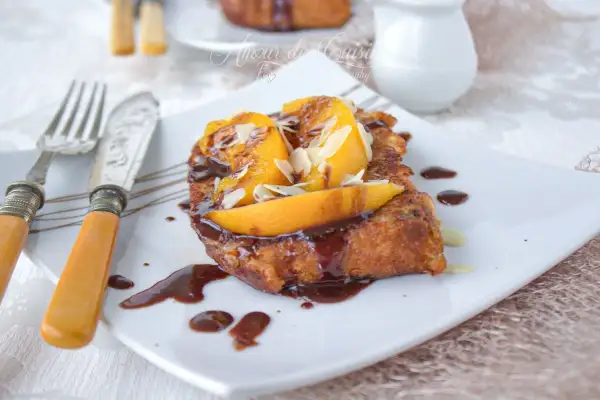 Une délicieuse brioche perdue, nappée de chocolat et garnie de fruits et d'amandes effilées, prête à être dégustée.